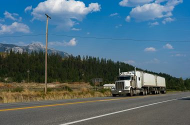 A white semi-truck traveling on a scenic road in Jaffray, BC, with mountains in the background.